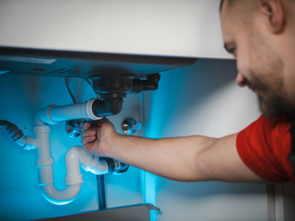 Technician working under a sink to inspect and clear waste pipe connections